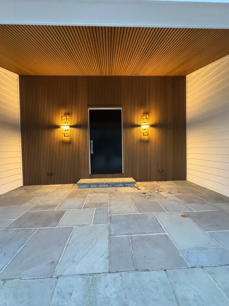 Entry with wood slat walls and ceiling, lit by wall sconces